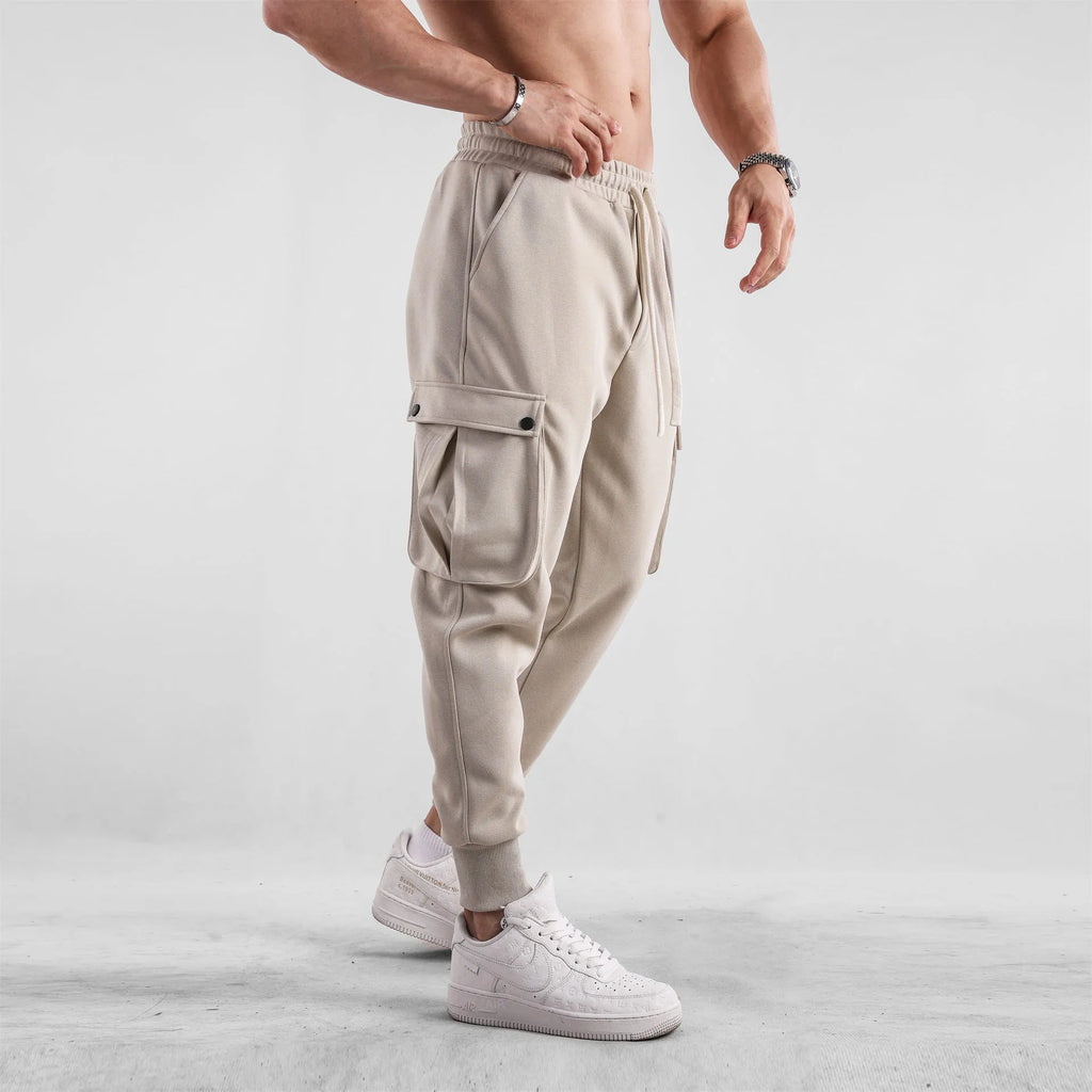 Man wearing loose light grey cotton trousers with ankle tie and multiple pockets, style of American sports leisure wear.