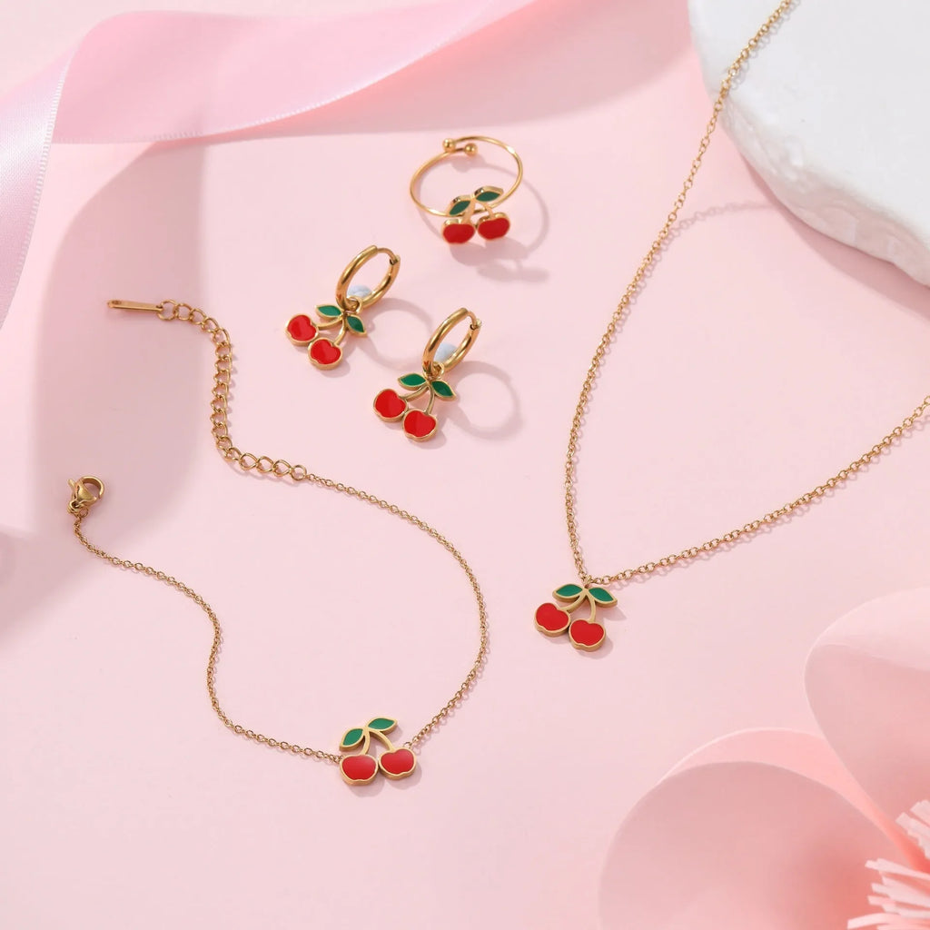 Cherry-themed jewellery set showing stainless steel necklace, bracelet, earrings, and ring with 18K gold plating.