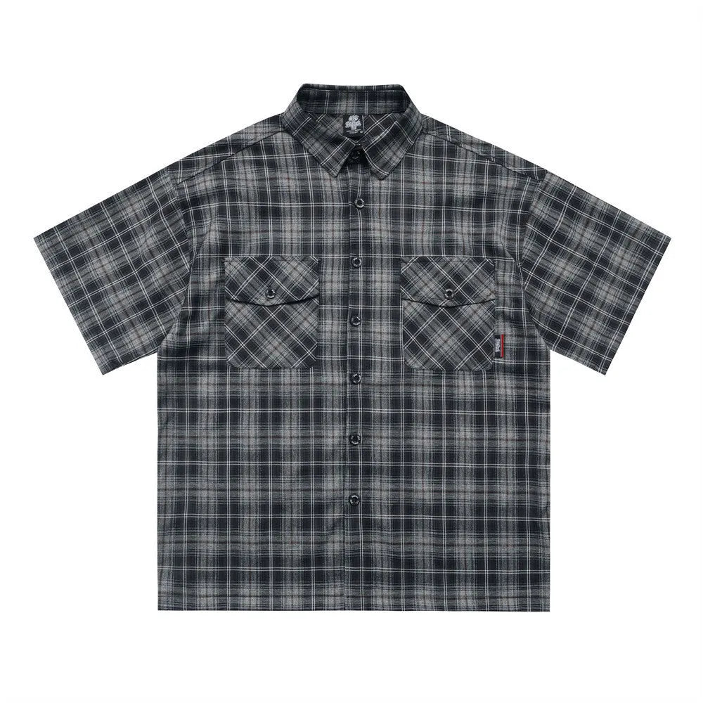 Man wearing a black and brown plaid short sleeve shirt with embroidered letters on the lapel