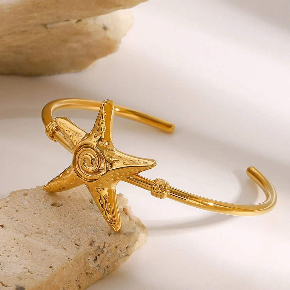 Stainless steel open-ended bracelet with starfish charm on a flat surface