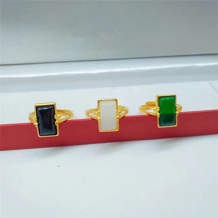 Adjustable brass gold-plated ring with a central green artificial gemstone on a finger.