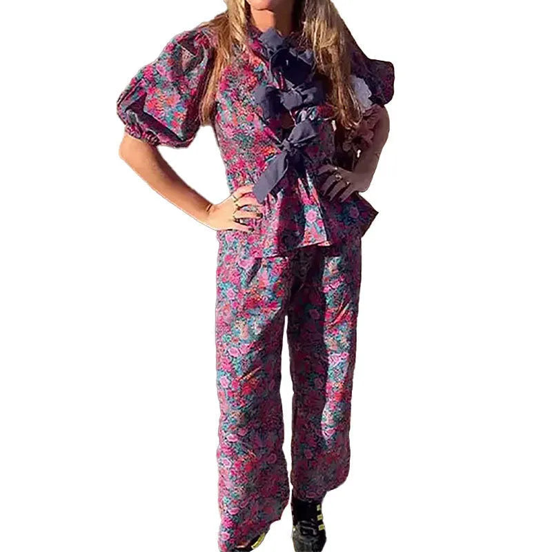Floral print two-piece leisure suit with tie-neck blouse, puff sleeves, and long trousers.
