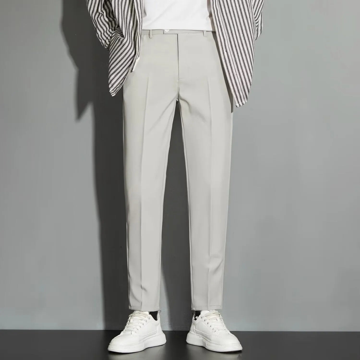 Man wearing straight leg ankle-length suit trousers in a light colour, showing the drape of the fabric.