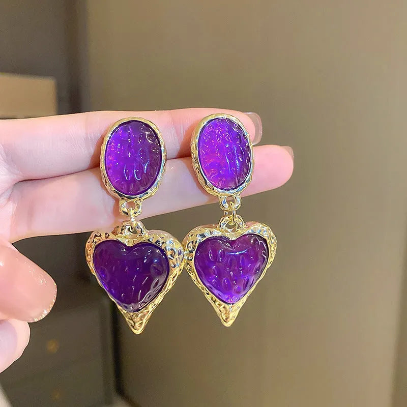 Oval-shaped love heart stud earrings with a pleated silver texture in purple, red, green, and yellow/white colours.