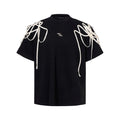 Black loose fit short sleeve T-shirt with ribbon and rivet decorated padded shoulders.