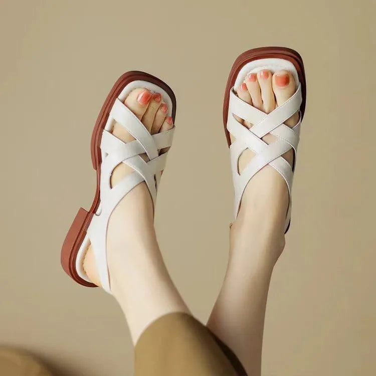 Women's glossy patent leather square-toe sandals with cross-strap fastening on a neutral background