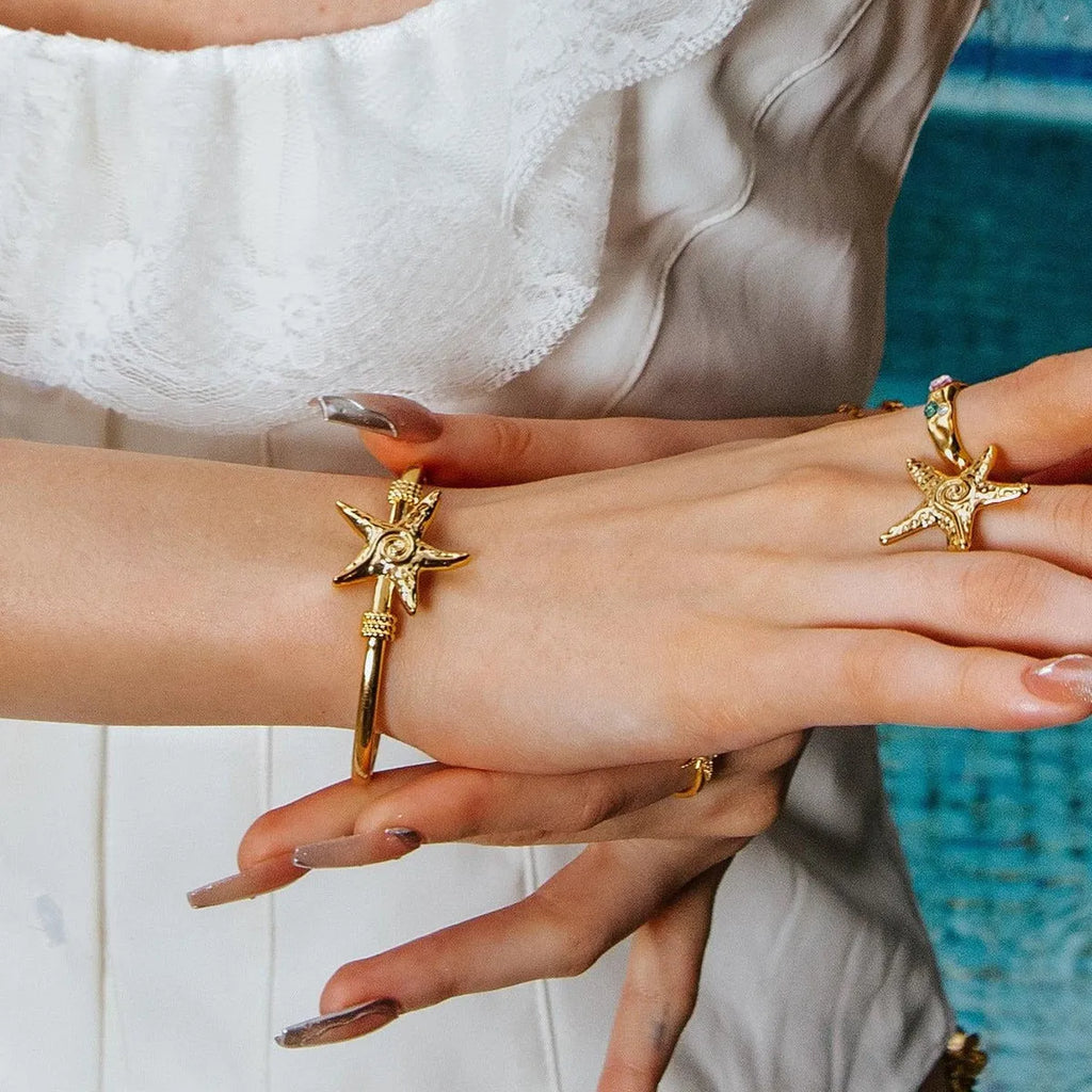 Stainless steel open-ended bracelet with starfish charm on a flat surface