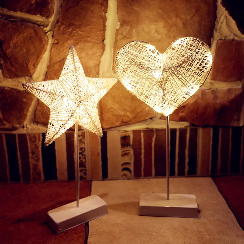 Rattan and copper wire LED table lamp in a star, heart, or moon shape on a wooden table.