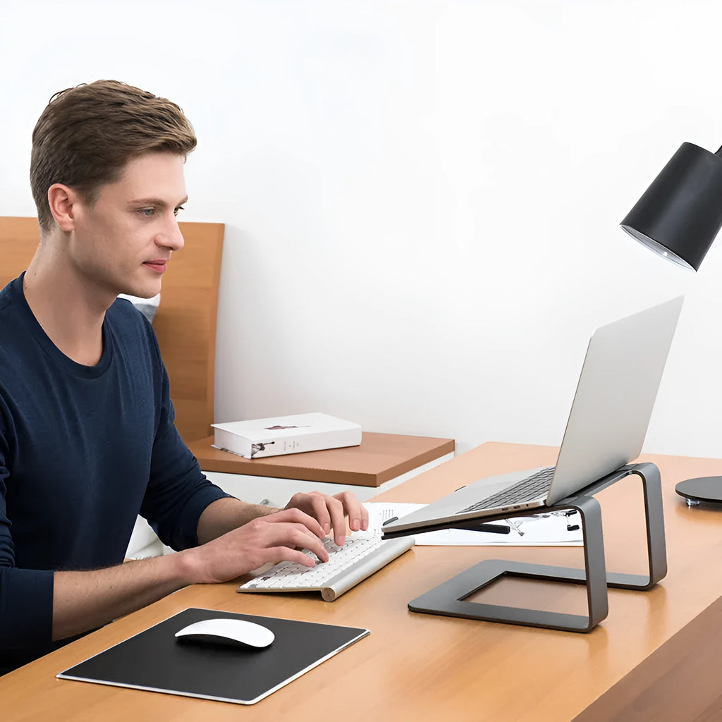 Black aluminium laptop stand on desk supporting silver laptop at improved viewing height