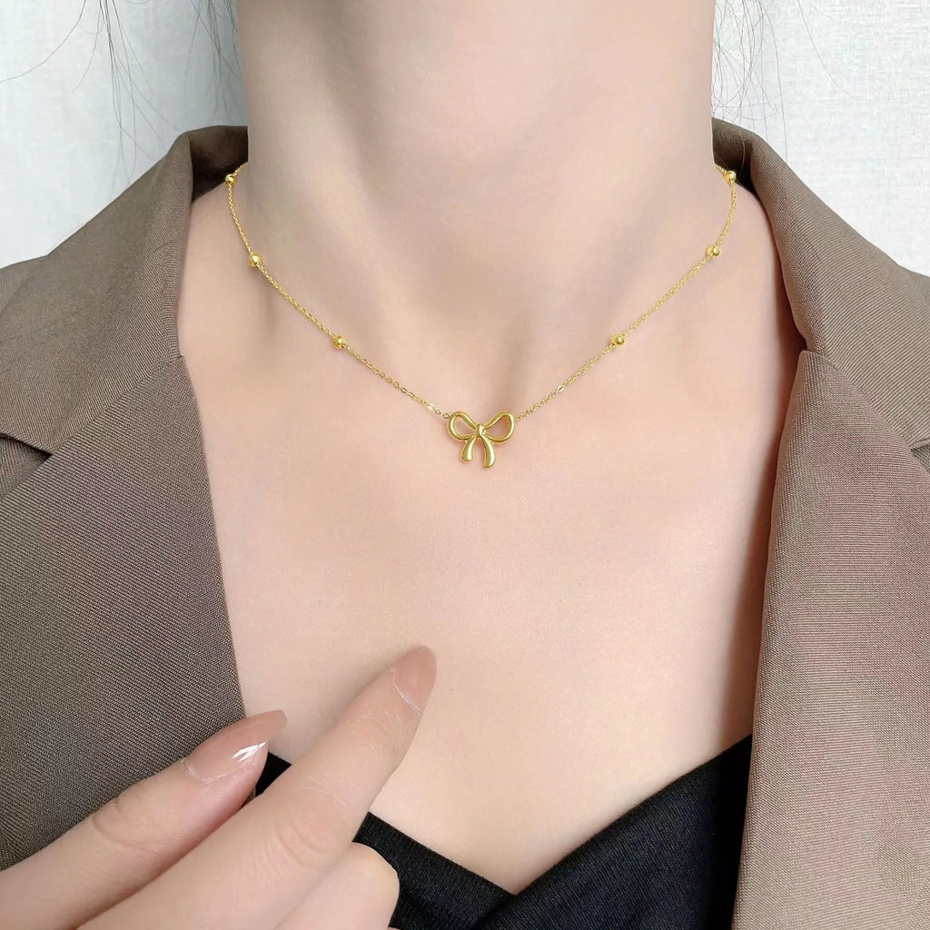 Gold electroplated bow necklace with adjustable chain on dark background