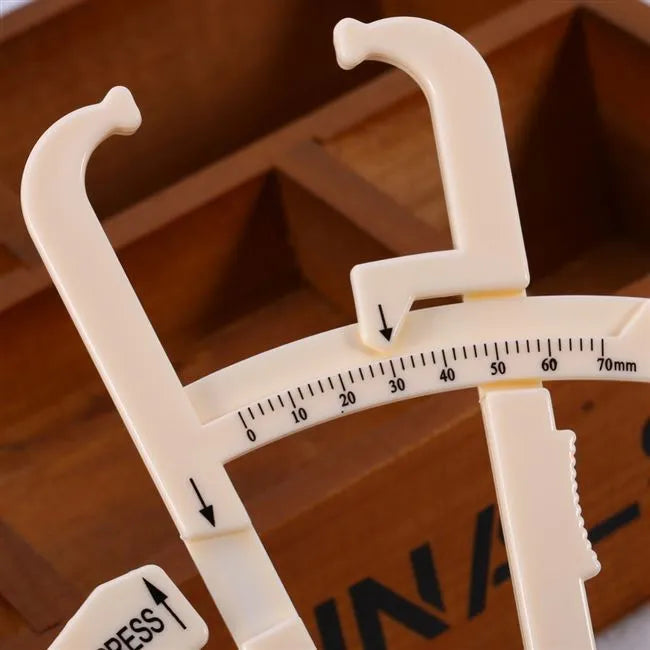 Transparent acrylic body fat caliper with measurement scale on a white background.