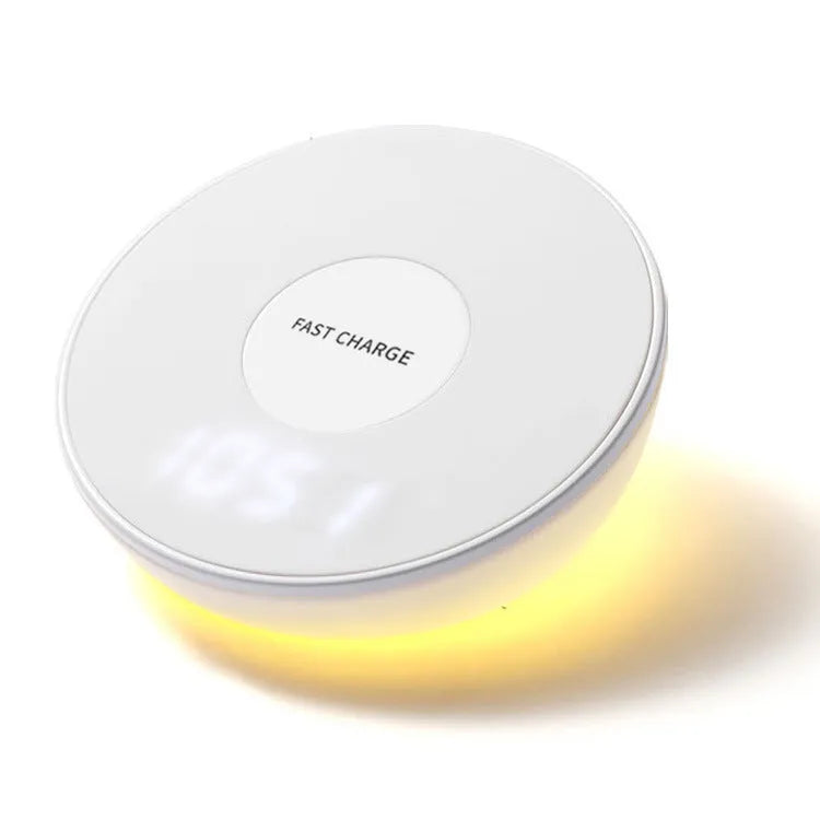 White Qi wireless charger with digital clock display on a desk next to a mobile phone.