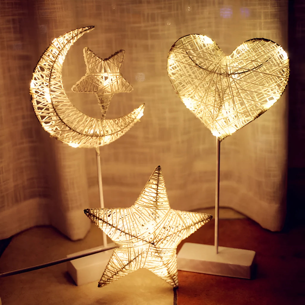 Rattan and copper wire LED table lamp in a star, heart, or moon shape on a wooden table.