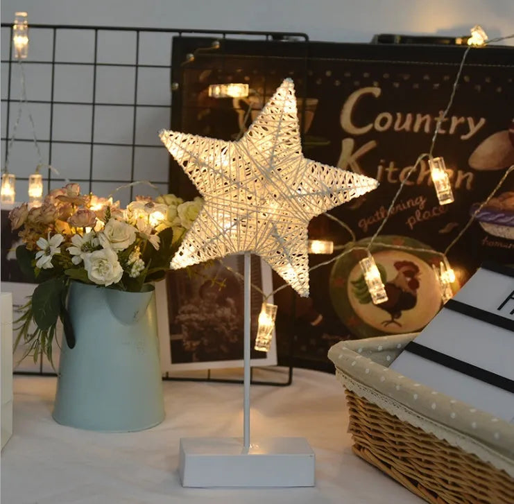 Rattan and copper wire LED table lamp in a star, heart, or moon shape on a wooden table.