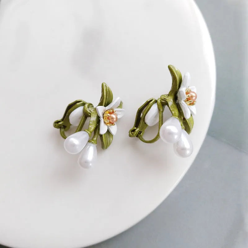 A pair of women's earrings showing sterling silver camellia flower studs and a matching alloy flower clip on a white background.