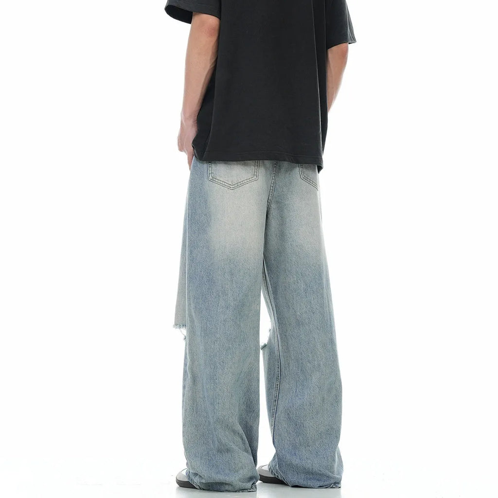 Man wearing blue straight-leg jeans with ripped detailing and an adjustable waistband.