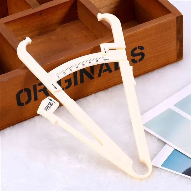 Transparent acrylic body fat caliper with measurement scale on a white background.