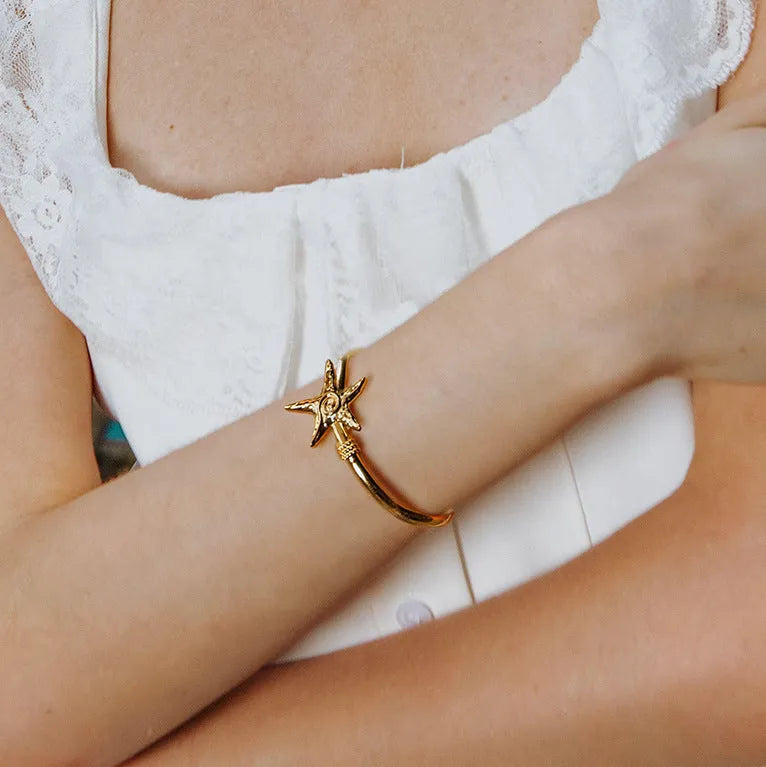 Stainless steel open-ended bracelet with starfish charm on a flat surface