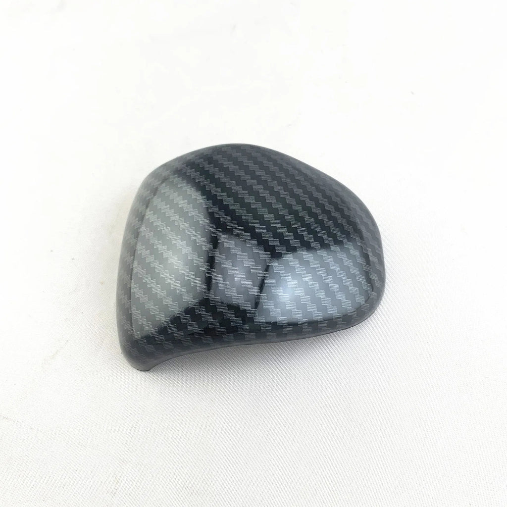 Black gear shift cover with a carbon fibre pattern for car interior styling.