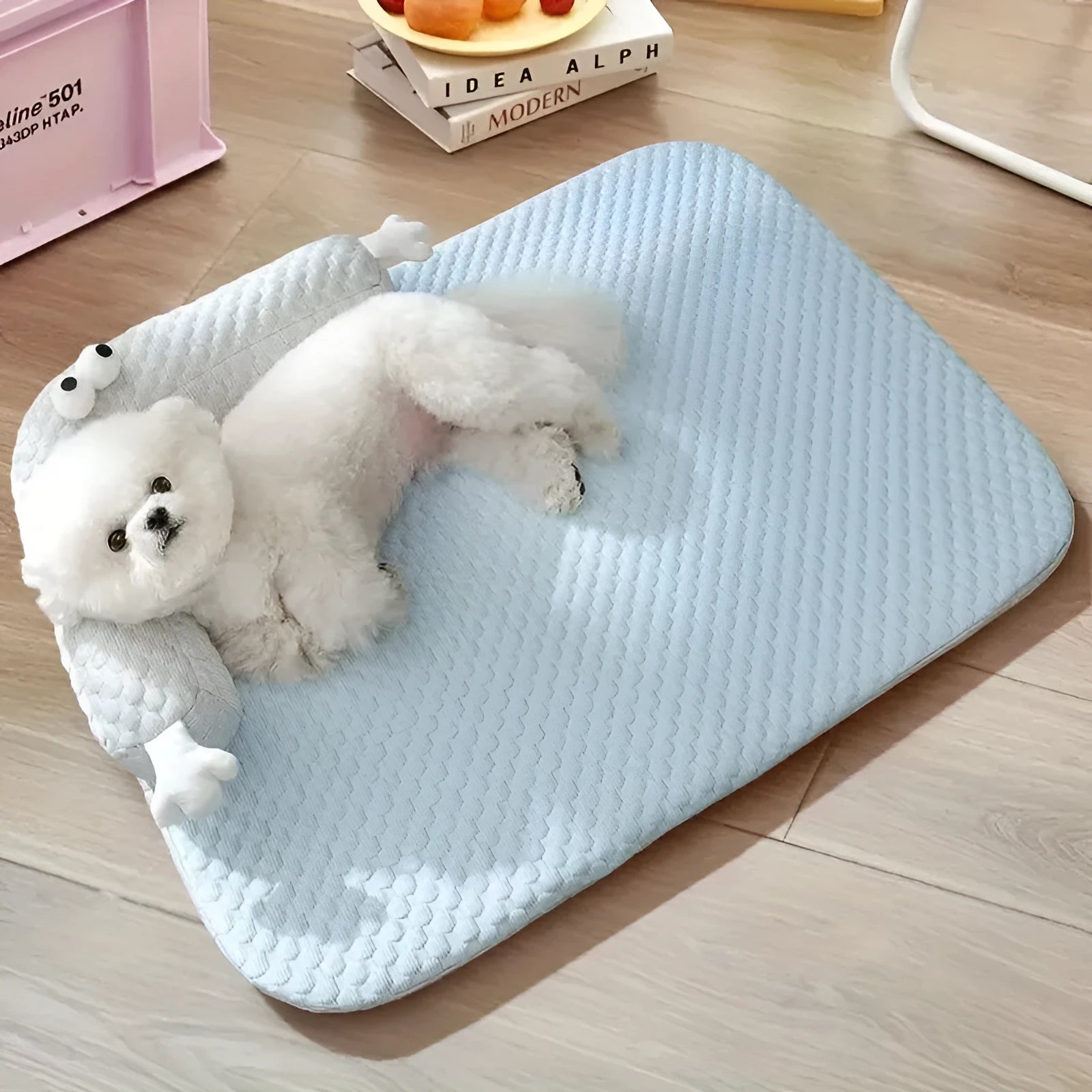 Blue pet bed cushion with a big-eyed monster design on a wooden floor.