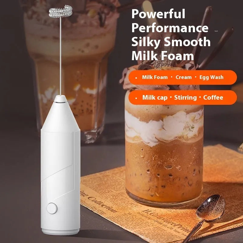 Compact black handheld USB rechargeable milk frother with stainless steel whisk on a kitchen counter.