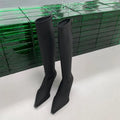 Black pointed toe below knee stiletto heel boots with a back zipper on a woman's leg.