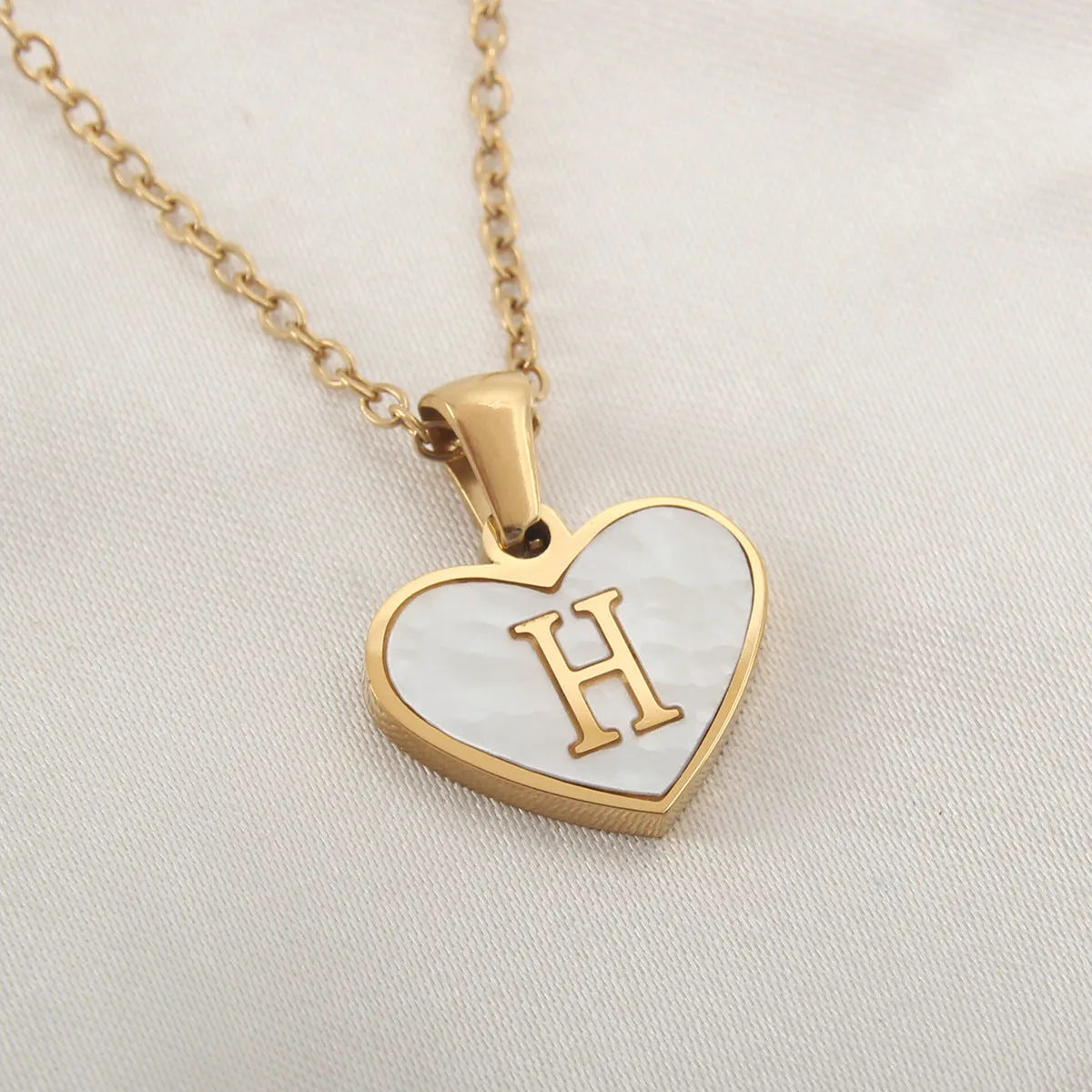 Gold-plated heart necklace with white shell pendant personalised with a letter, on an adjustable chain.