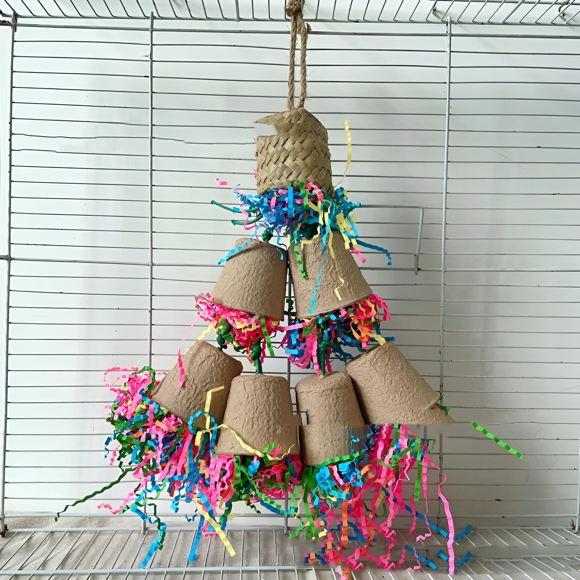 Parrot chew toy with woven palm fibres and a paper cup, hanging 38 cm long in a natural wood colour.