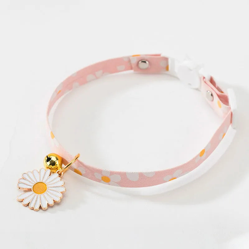 Green adjustable cat collar with a metal bell and a pink bow tie attached, shown on a measuring tape indicating size