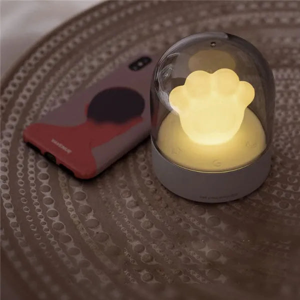 Grey or pink cat paw shaped USB rechargeable night light with music box function on a desk.