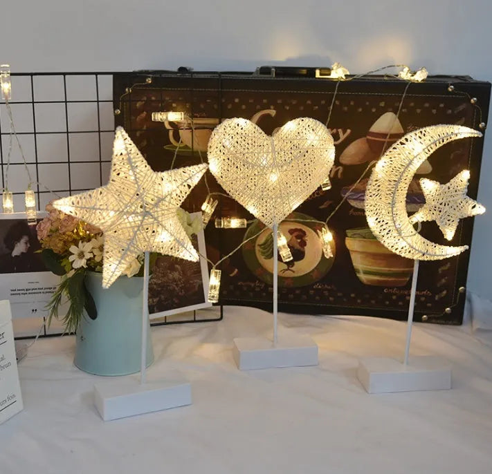 Rattan and copper wire LED table lamp in a star, heart, or moon shape on a wooden table.
