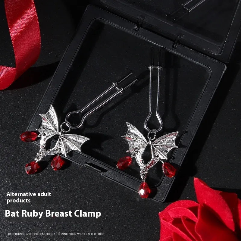 Silver bat-shaped nipple clamp with ruby gemstone and adjustable mechanism.