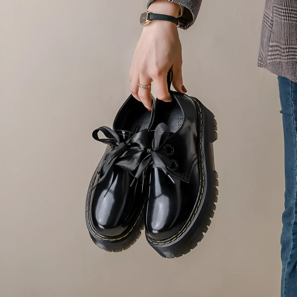 Women's black thick soled lace-up shoes with ribbon detail on a white background
