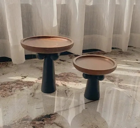 Round natural wooden tray with high legs holding a candle and perfume bottle on a table.