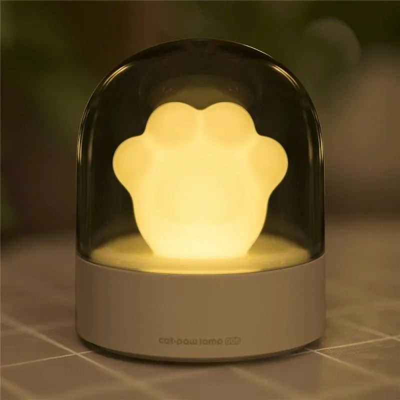 Grey or pink cat paw shaped USB rechargeable night light with music box function on a desk.