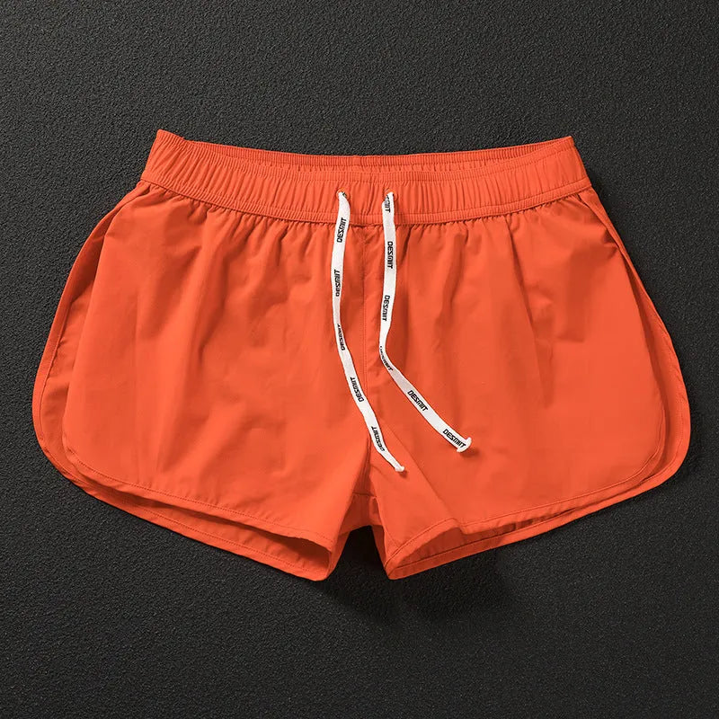 Man wearing loose orange red polyester shorts on a beach, demonstrating the micro-elastic fit.