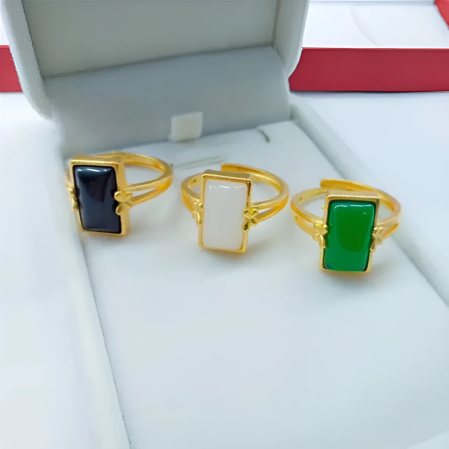 Adjustable brass gold-plated ring with a central green artificial gemstone on a finger.