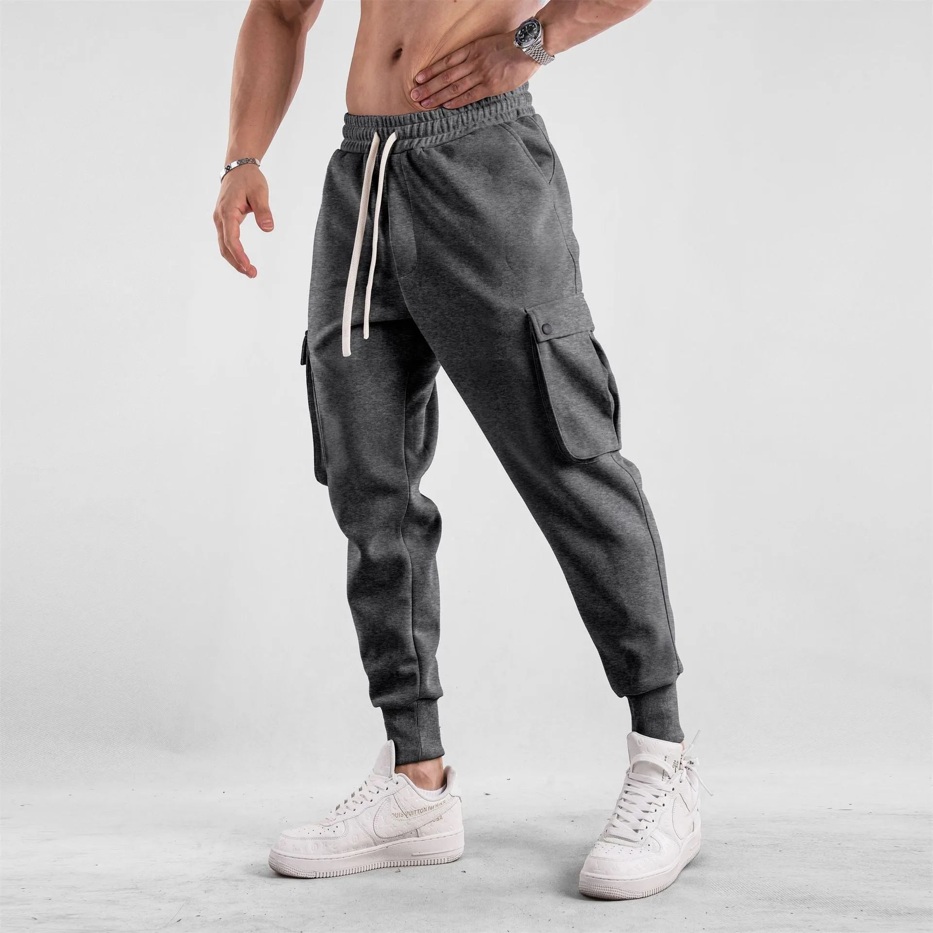 Man wearing loose light grey cotton trousers with ankle tie and multiple pockets, style of American sports leisure wear.
