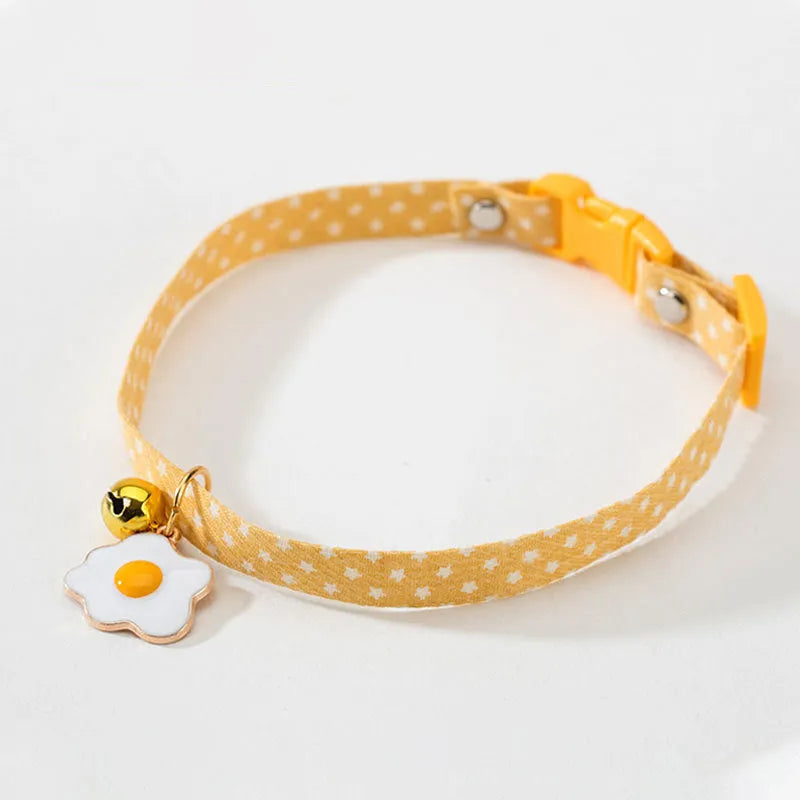 Green adjustable cat collar with a metal bell and a pink bow tie attached, shown on a measuring tape indicating size
