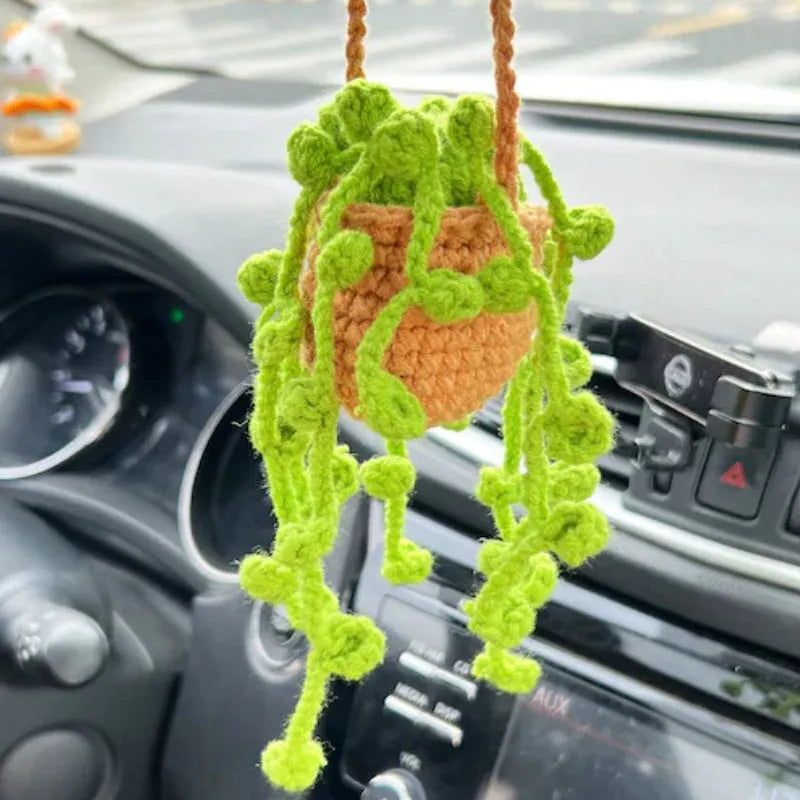 Green and white knitted wool car plant decoration with hanging rope on car dashboard
