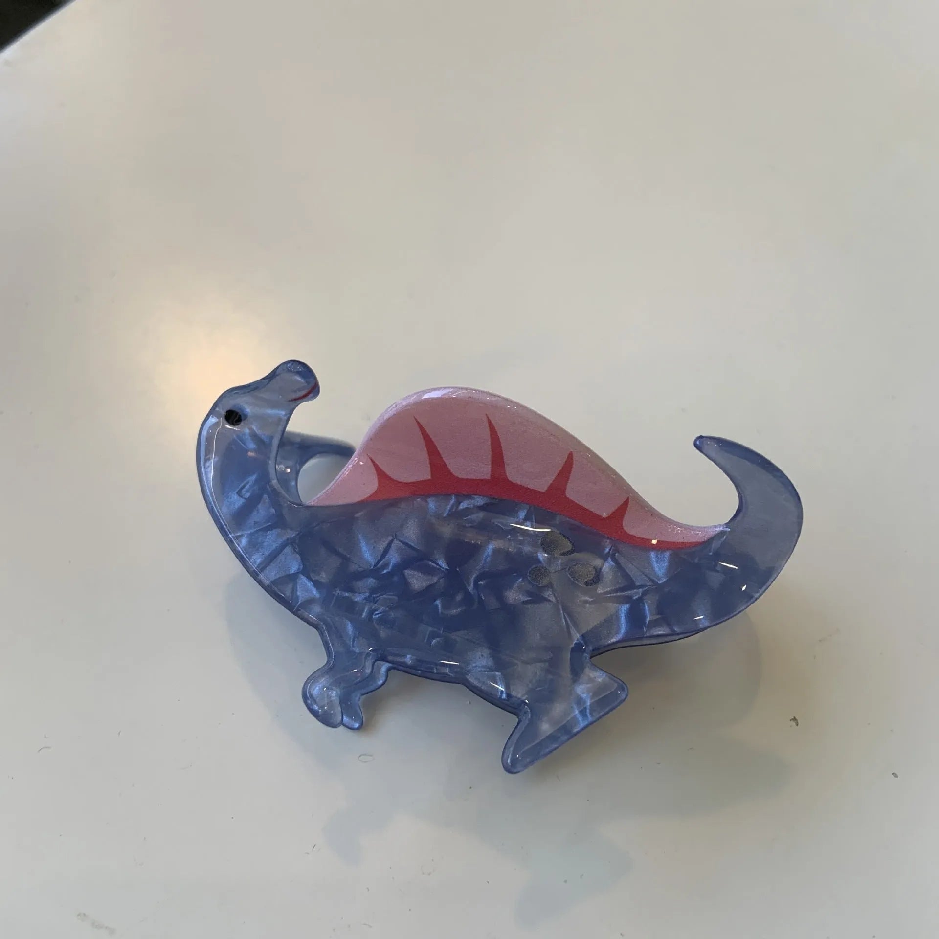 A colourful acrylic jaw clip hair grip featuring a detailed little dinosaur design.