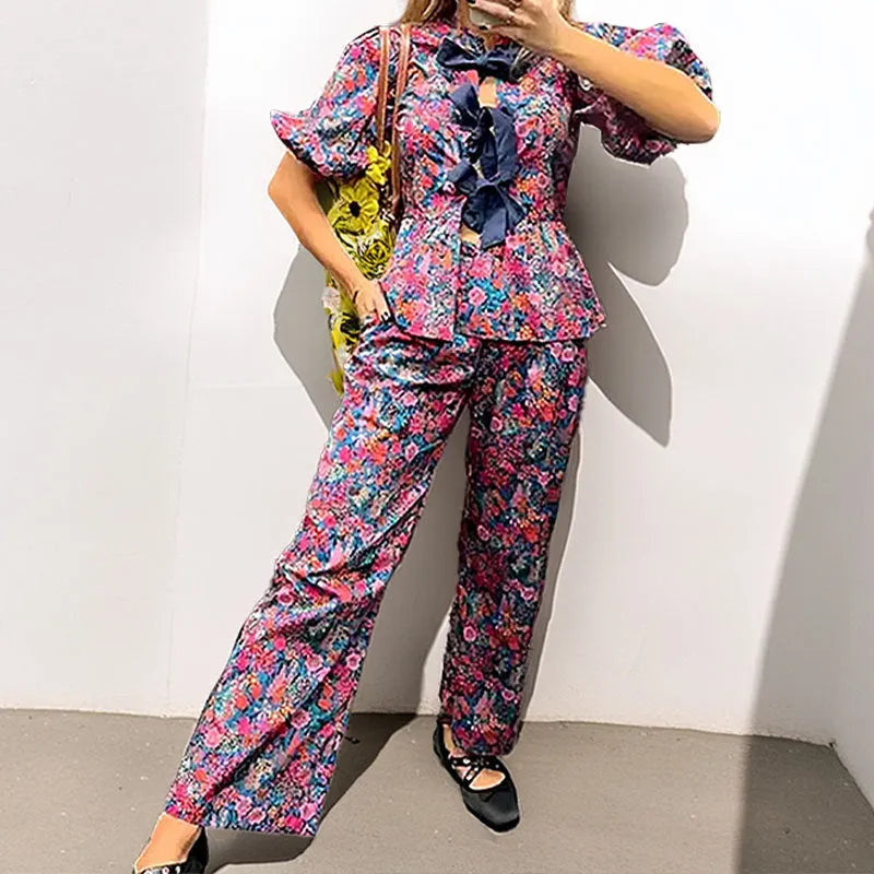 Floral print two-piece leisure suit with tie-neck blouse, puff sleeves, and long trousers.