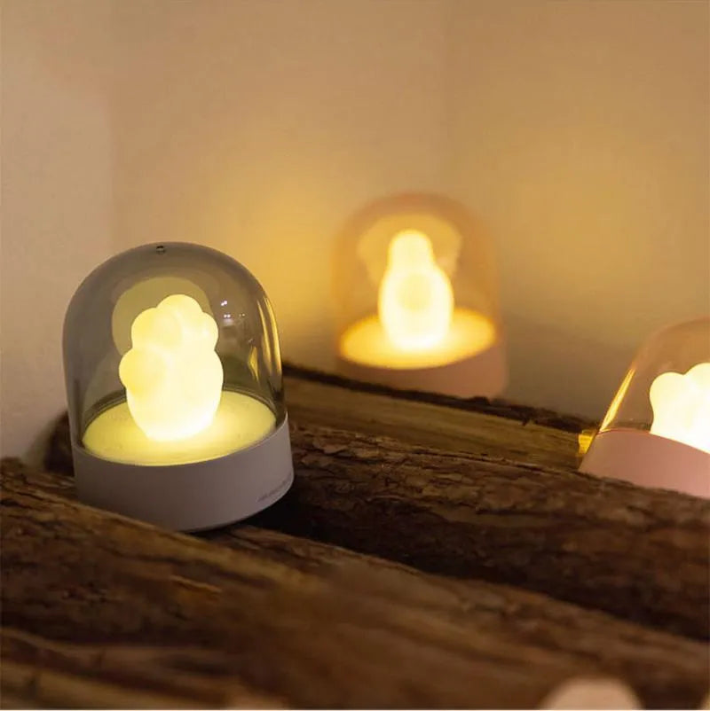 Grey or pink cat paw shaped USB rechargeable night light with music box function on a desk.