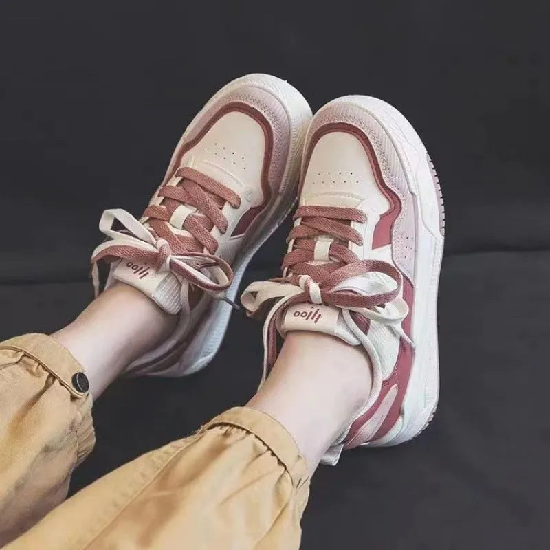 Pink and beige low top women's sneakers with a rubber sole on a neutral background.