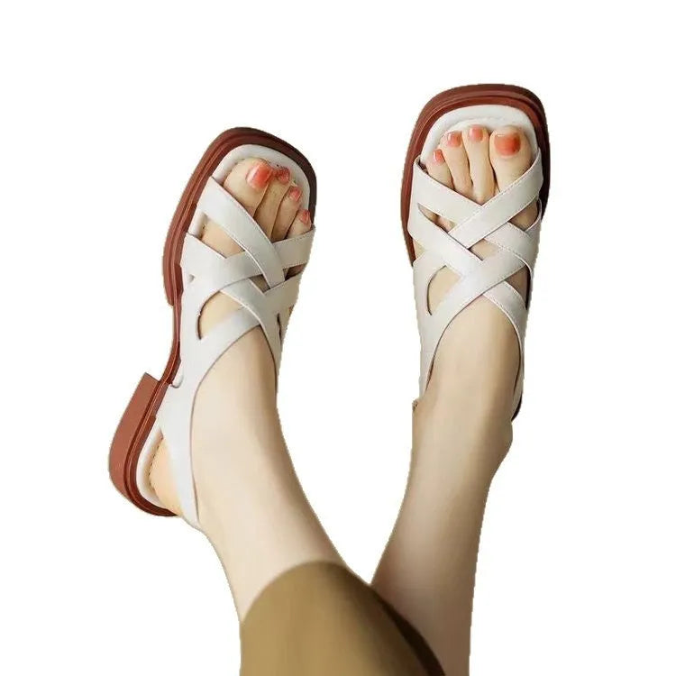 Women's glossy patent leather square-toe sandals with cross-strap fastening on a neutral background