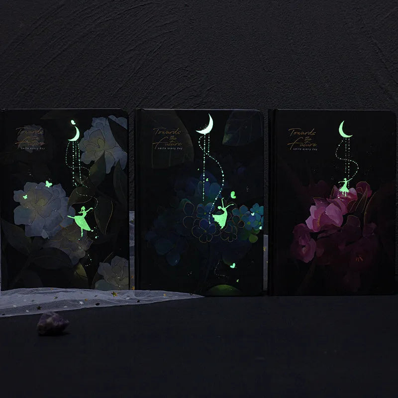 A5 notebook with a luminous cover open to show internal colour illustrations, next to Purple, Light Blue, Gold, and Deep Blue colour options.