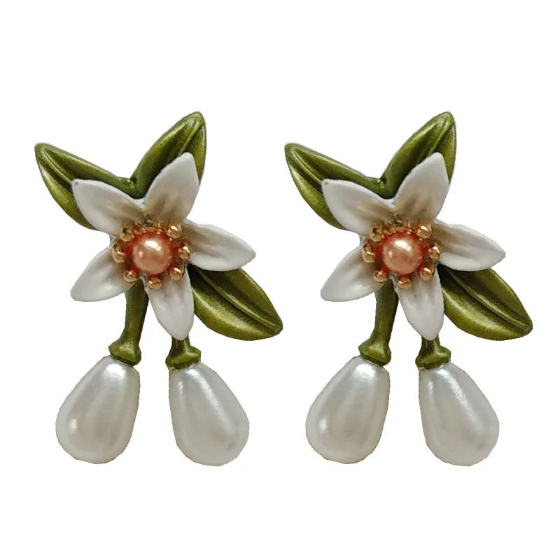 A pair of women's earrings showing sterling silver camellia flower studs and a matching alloy flower clip on a white background.