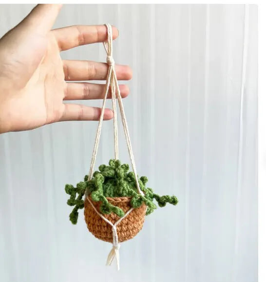 Green and white knitted wool car plant decoration with hanging rope on car dashboard