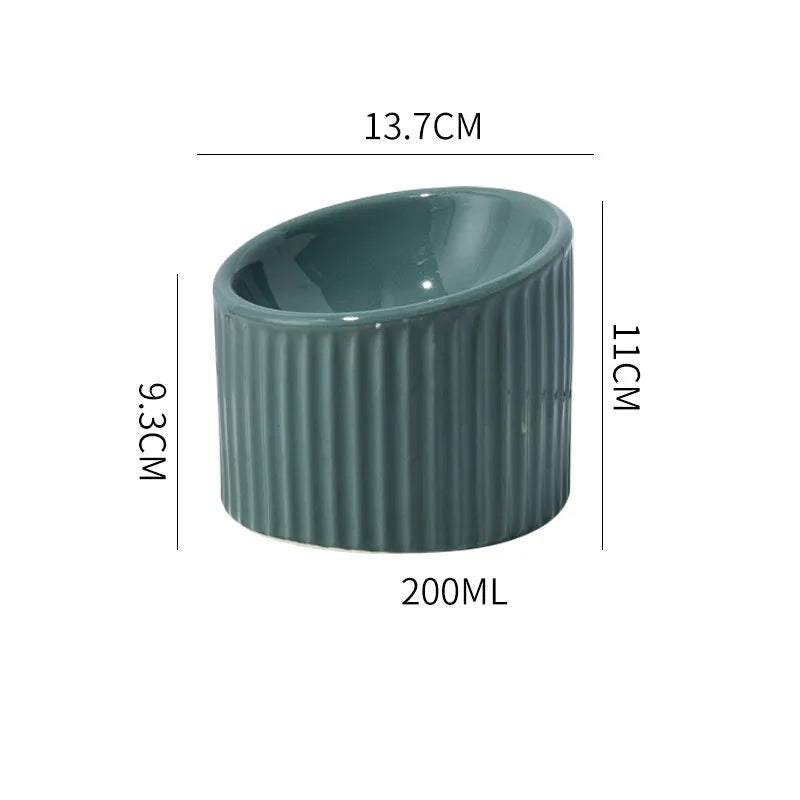 Dark green elevated ceramic cat bowl on a wooden floor, showing its raised height and round, whisker-friendly shape.