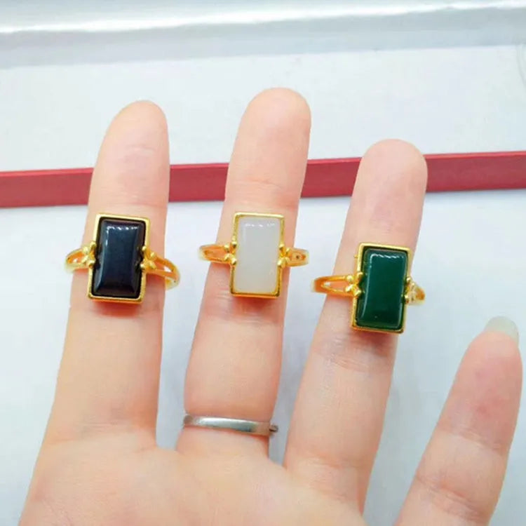 Adjustable brass gold-plated ring with a central green artificial gemstone on a finger.